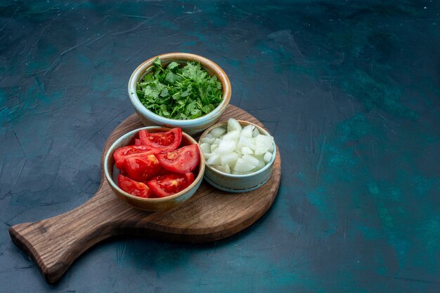 Vista frontal de verduras frescas en rodajas, tomates y cebollas con verduras en un plato de verduras de cena de comida de escritorio azul oscuro