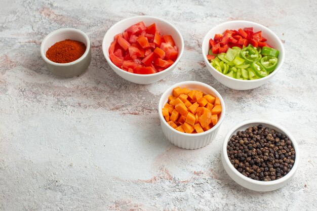 Vista frontal de verduras en rodajas con pimientos sobre la superficie blanca