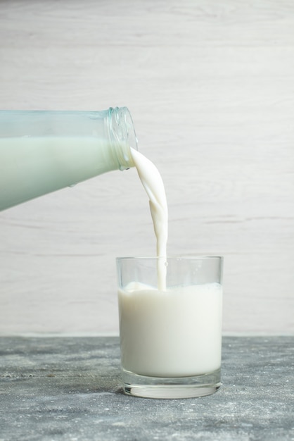 Vista frontal verter leche en el vaso pequeño en blanco, beber leche de leche cremosa