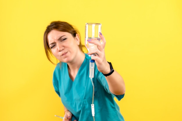 Vista frontal del veterinario femenino que sostiene el gotero en el piso amarillo animal de salud del animal doméstico