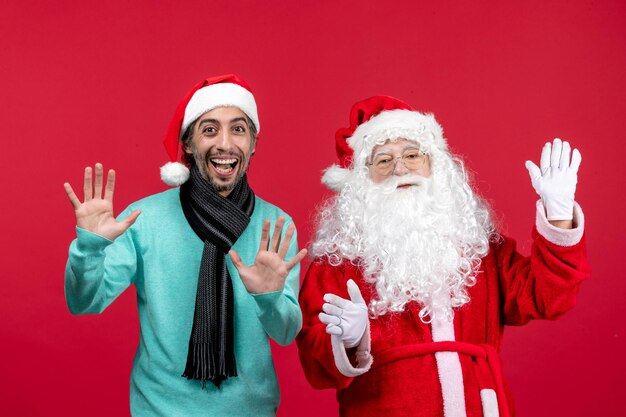 Vista frontal del viejo Papá Noel con el hombre de pie en la pared roja