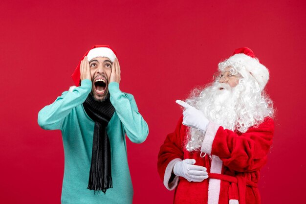 Vista frontal del viejo Papá Noel con el hombre de pie en la pared roja