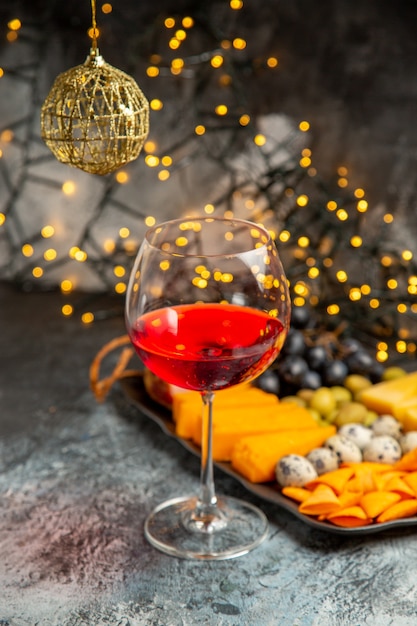 Vista frontal del vino tinto seco en un vaso junto a la merienda sobre fondo gris