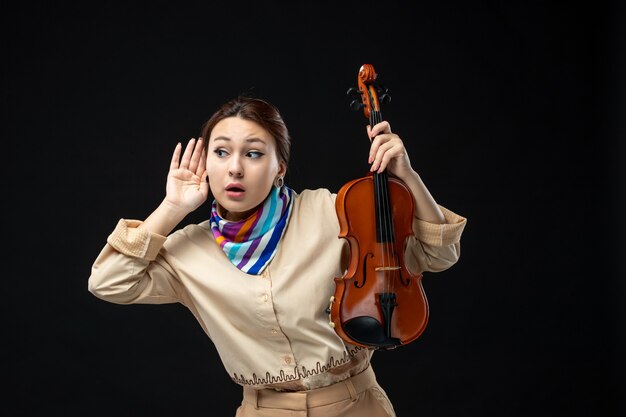 Vista frontal violinista sosteniendo su violín en la pared oscura música concierto melodía instrumento mujer actuación emoción juega