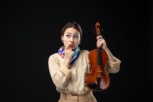 Vista frontal violinista sosteniendo su violín pensando en la pared oscura música concierto instrumento mujer emoción tocar melodía rendimiento