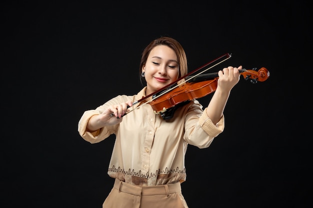 Vista frontal violinista tocando el violín en la pared oscura instrumento musical tocar melodía emoción mujer