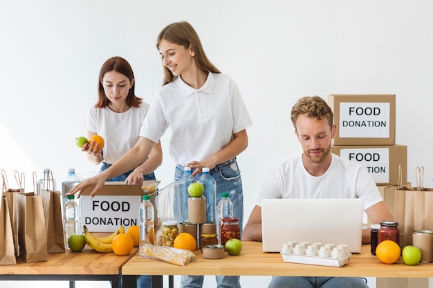 Foto gratuita vista frontal de voluntarios con cajas de donación de alimentos y computadora portátil