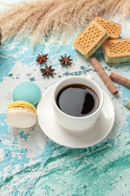 Vista frontal de waffles y macarons con una taza de té en la superficie azul de la galleta de la torta de la galleta dulce de azúcar