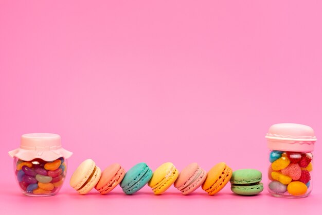 Una vista frotn macarons franceses junto con caramelos multicolores dentro de latas en rosa