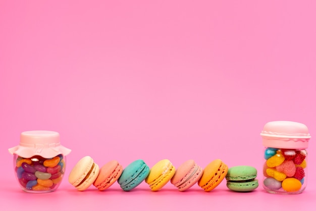 Una vista frotn macarons franceses junto con caramelos multicolores dentro de latas en rosa