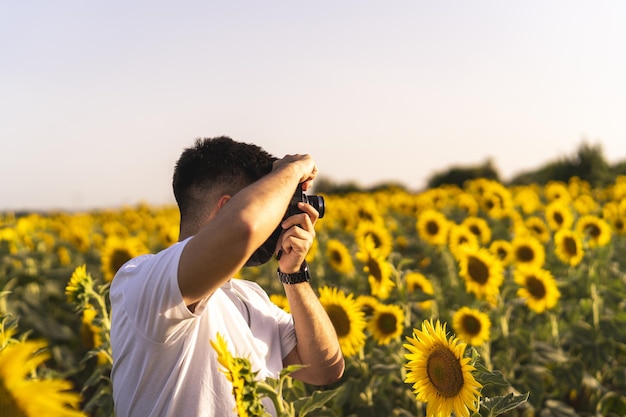 Vista de un hombre caucásico con una máscara negra tomando fotos de una persona en el campo de girasoles