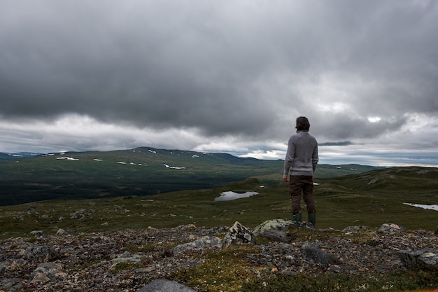 Vista de un hombre de pie sobre una colina rocosa con nubes tormentosas