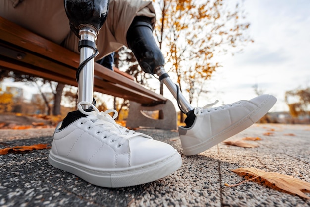 Vista de un hombre con piernas ortopédicas y zapatillas blancas sentado en un banco en un parque