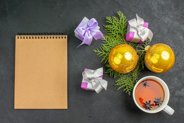 Vista horizontal de coloridos regalos una taza de té negro y accesorios de decoración portátil sobre fondo oscuro