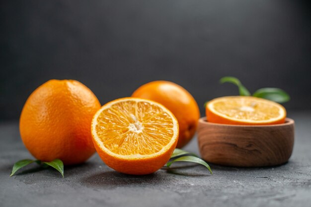 Vista horizontal del conjunto de naranjas frescas enteras y cortadas por la mitad en la mesa oscura