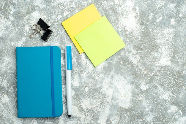 Vista horizontal del cuaderno azul cerrado y bolígrafo coloridos papeles de nota sobre fondo blanco.