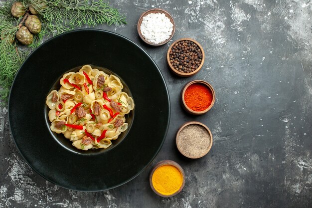 Vista horizontal de deliciosa conchiglie con verduras y verduras en un plato y cuchillo y diferentes especias sobre fondo gris