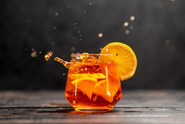 Vista horizontal de delicioso jugo fresco en un vaso con limas de naranja en la mesa oscura