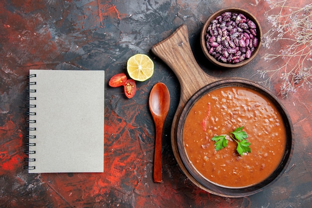 Vista horizontal de frijoles de sopa de tomate y portátil en la tabla de cortar en una tabla de colores mezclados