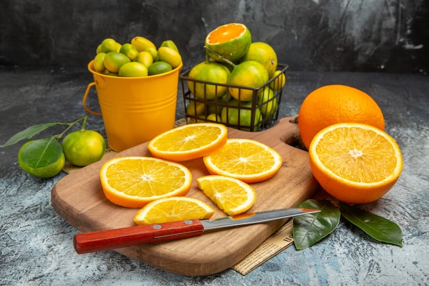 Vista horizontal de frutas cítricas frescas con un cuchillo sobre la tabla de cortar de madera en el periódico sobre fondo gris