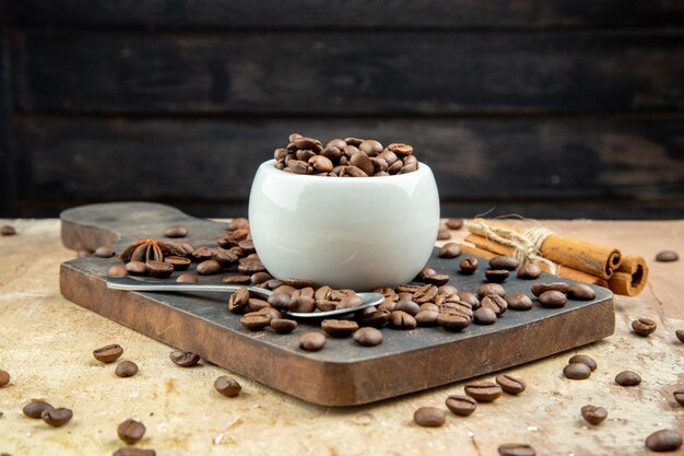 Vista horizontal de los granos de café dentro y fuera de un pequeño tazón blanco sobre una tabla de madera sobre fondo de color mezclado
