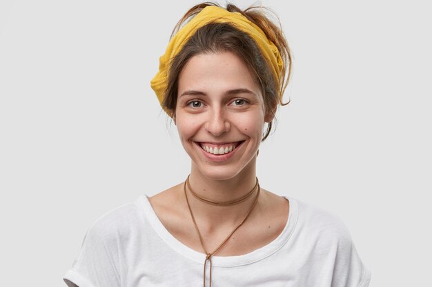 Vista horizontal de una mujer atractiva con apariencia europea, tiene una sonrisa tierna, se alegra de tener un día libre después de una dura semana de trabajo, tiene el cabello oscuro peinado