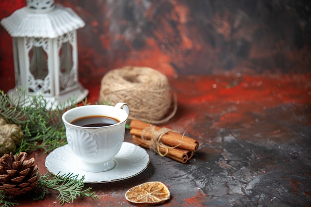 Vista horizontal de ramas de abeto canela limas cono de coníferas una bola de cuerda una taza de té negro sobre fondo rojo.