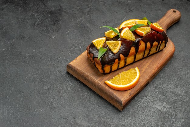 Vista horizontal de sabrosos pasteles decorados con naranjas y chocolate en la tabla de cortar en el cuadro negro