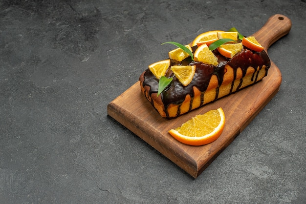 Vista horizontal de sabrosos pasteles decorados con naranjas y chocolate en la tabla de cortar en el cuadro negro