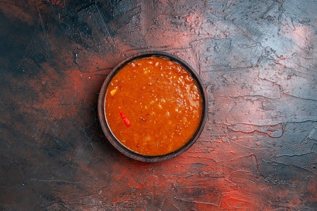 Foto gratuita vista horizontal de la sopa de tomate en un recipiente marrón sobre una mesa de colores mezclados