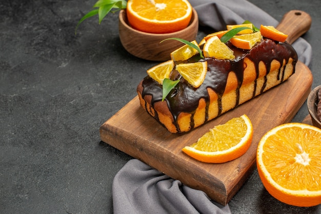 Vista horizontal de suaves y sabrosos pasteles cortan naranjas con galletas en una tabla de cortar de madera y una toalla
