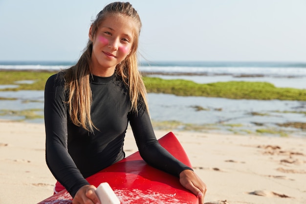 Foto gratuita vista horizontal de surfista profesional se prepara para el surf, tabla de cera con cera, quiere demostrar doble hilandero