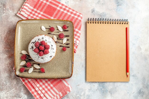 Vista horizontal de tarta recién horneada con frambuesas y cuaderno con lápiz