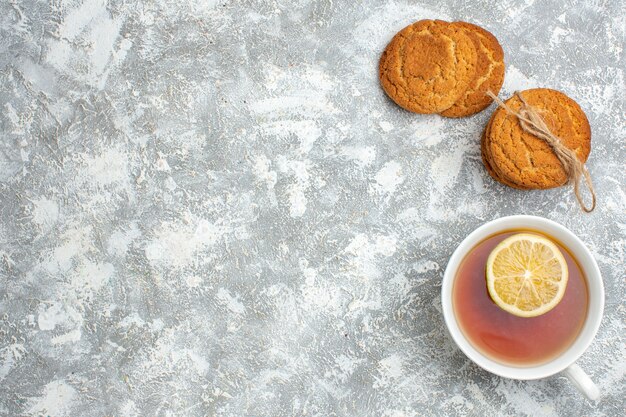 Vista horizontal de una taza de té negro con limón y deliciosas galletas sobre la superficie del hielo