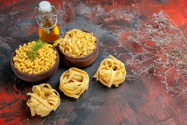 Vista horizontal de varios tipos de pastas crudas y botella de aceite en la tabla de colores mezclados