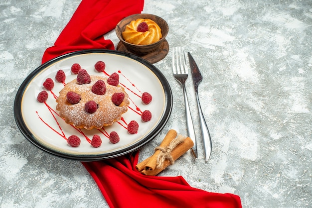 Vista inferior baya pastel en placa ovalada blanca mantón rojo tenedor de galleta y cuchillo de cena en superficie gris