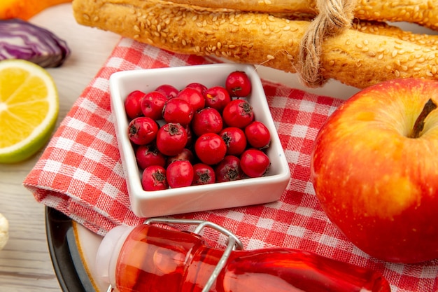 Vista inferior de las bayas de rosa de perro en un tazón de pan de manzana botella roja sobre una servilleta en un plato redondo sobre una mesa blanca