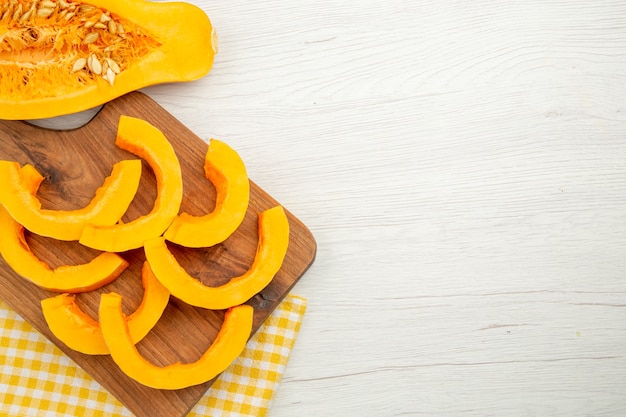 Vista inferior de la calabaza picada en una tabla de cortar sobre una toalla de cocina a cuadros blanco amarillo en el lugar libre de la mesa gris