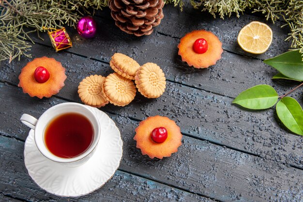 Vista inferior cereza cupcakes ramas de abeto rodaja de limón una taza de té galletas en la mesa de madera oscura.