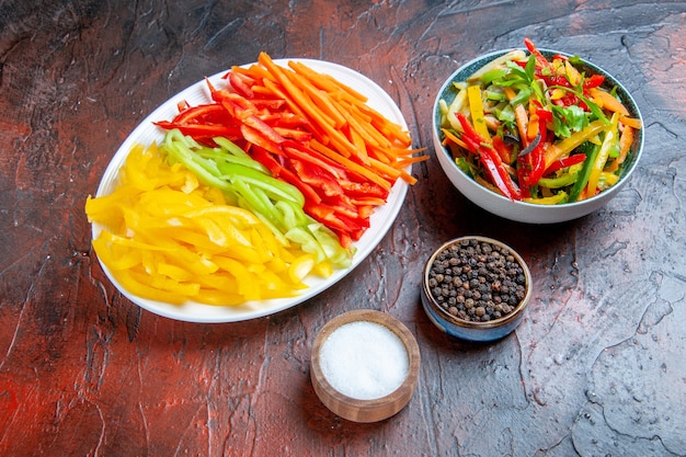 Vista inferior coloridos pimientos cortados en plato blanco ensalada de verduras en un tazón pimienta negra sal ajo en mesa rojo oscuro