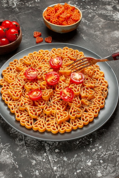 Vista inferior corazones de pasta italiana cortan tomates cherry en placa ovalada tenedor pasta corazón rojo en un tazón sobre mesa gris