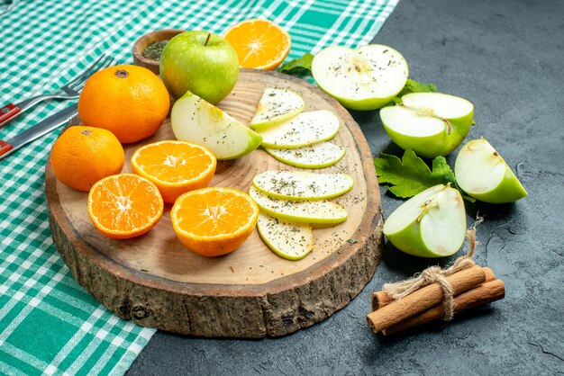 Vista inferior cortar manzanas y mandarinas con polvo de menta seca sobre tablero de madera palitos de canela sobre mantel verde sobre mesa oscura