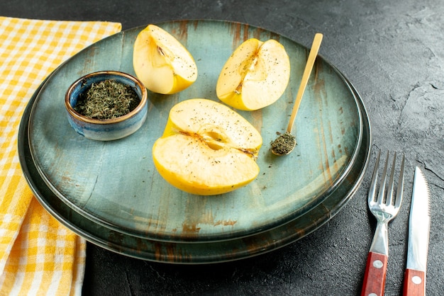 Vista inferior cortar las manzanas de menta seca en un tazón, cuchara de madera en un plato, cuchillo y un tenedor, toalla de cocina amarilla sobre suelo oscuro
