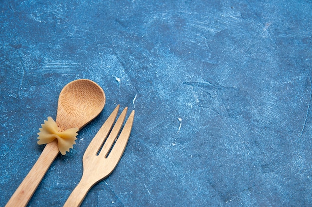 Vista inferior cuchara tenedor de madera farfalle en cuchara en el espacio libre de la mesa azul