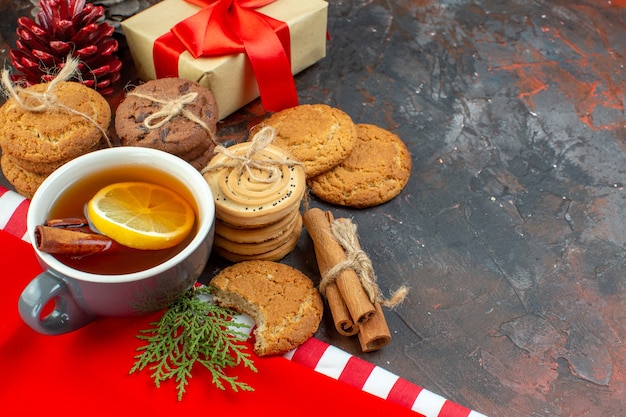 Vista inferior de diferentes galletas atadas con una cuerda taza de té, palitos de canela, regalo en el espacio libre de la mesa de color rojo oscuro