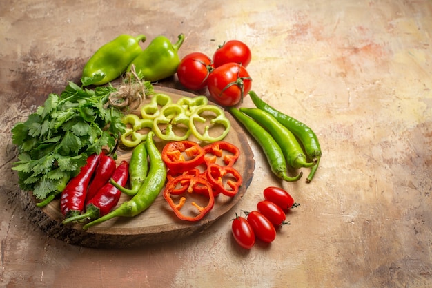 Vista inferior diferentes verduras cilantro pimientos picantes pimientos cortados en trozos en un tablero de madera de árbol redondo tomates cherry sobre fondo amarillo ocre espacio libre