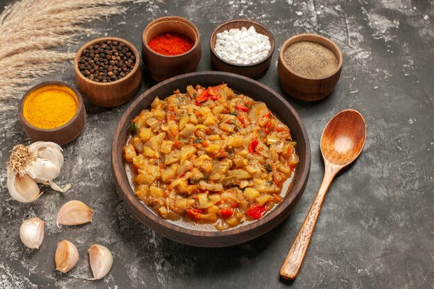 Vista inferior ensalada de berenjena asada en un tazón diferentes especias en tazones de madera cuchara de ajo en la mesa oscura