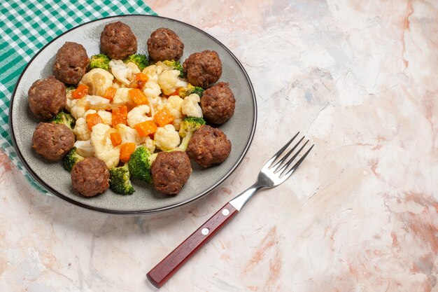 Vista inferior ensalada de brócoli y coliflor y albóndigas en un plato servilleta a cuadros verde y blanco un tenedor en lugar libre de fondo aislado desnudo