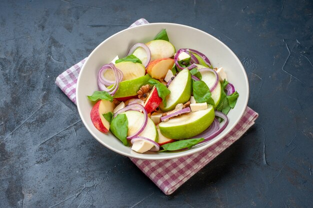 Vista inferior de la ensalada de manzana en un tazón de fuente rosa servilleta a cuadros blanco sobre la mesa oscura