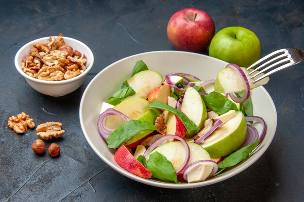 Vista inferior de la ensalada de manzana en un tazón rebanada de manzana en un tenedor nuez en un tazón manzanas rojas y verdes en una mesa aislada oscura